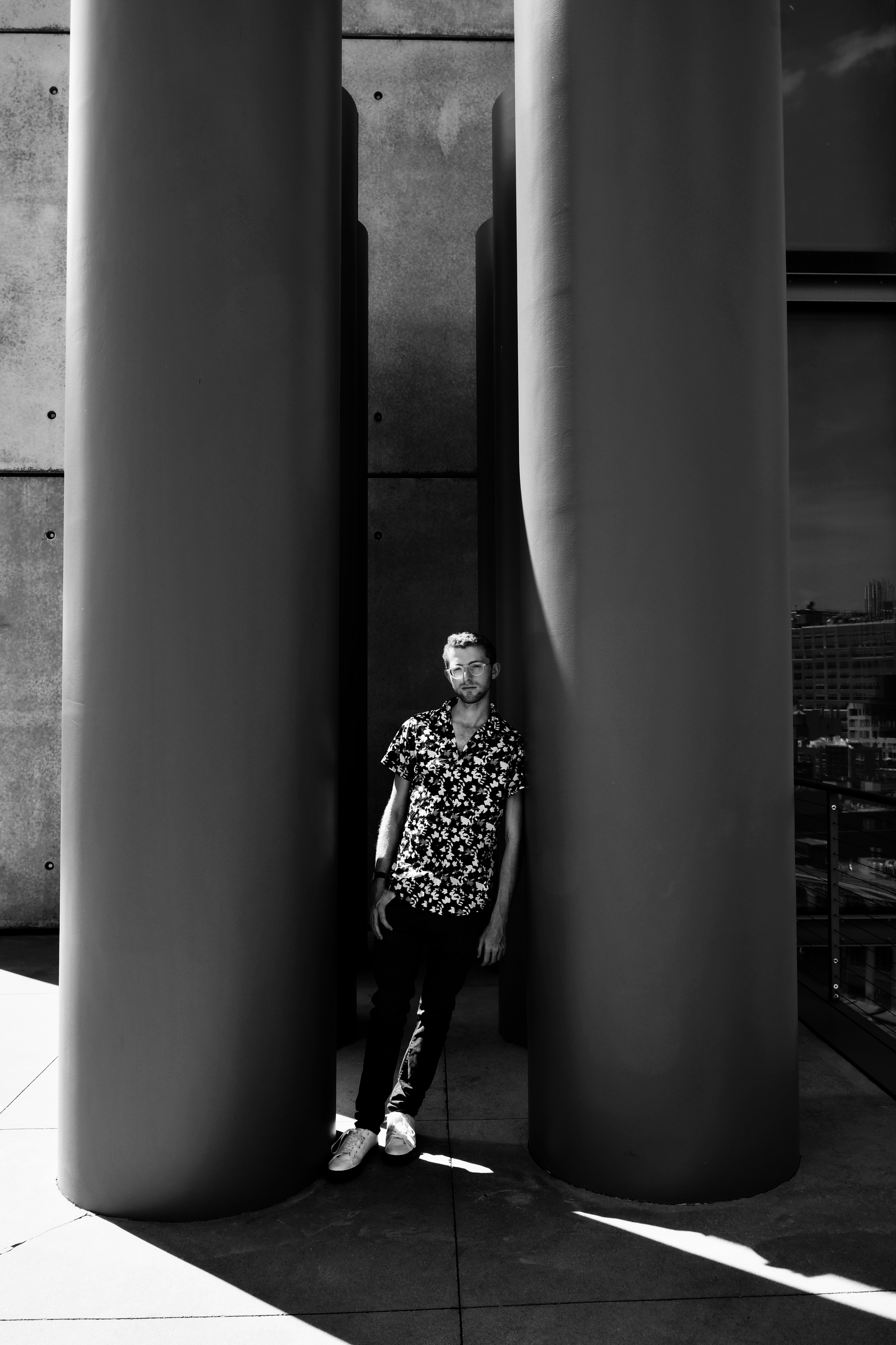 grayscale photo of man in black and white polka dot shirt and black pants standing beside